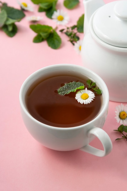 Cup of herbal tea with chamomile flowers and mint leaves on pink background
