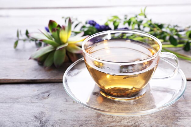 Cup of herbal tea with flowers on wooden table closeup