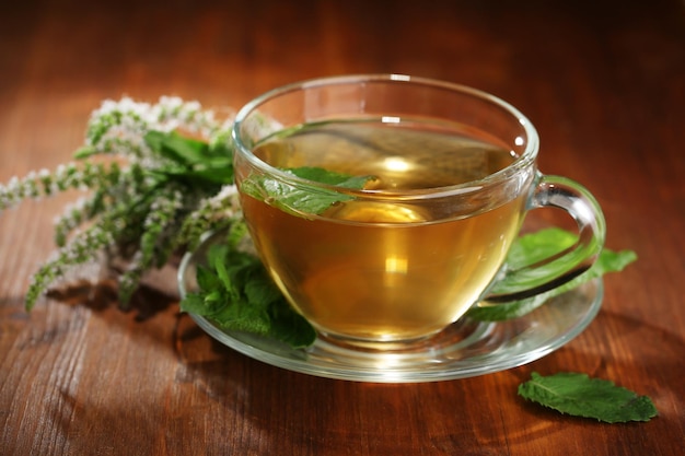 Cup of herbal tea with fresh mint flowers on wooden table