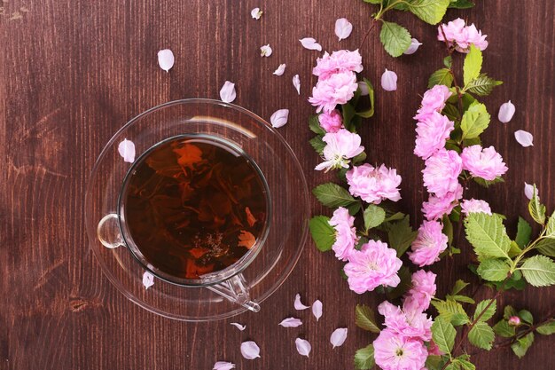 Cup of herbal tea with pink roses on wooden table top view