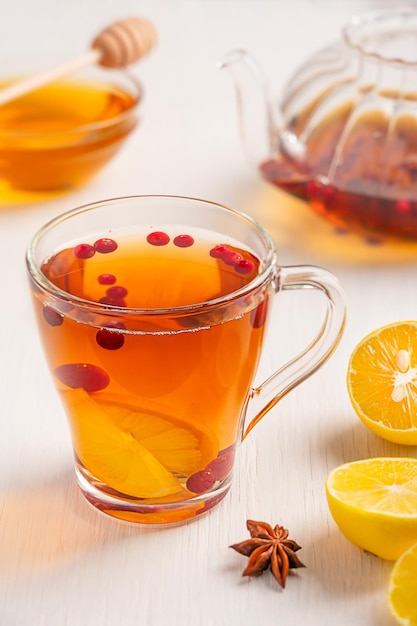 Cup of homemade herbal hot tea made with berries, lemon slices and honey served on white table