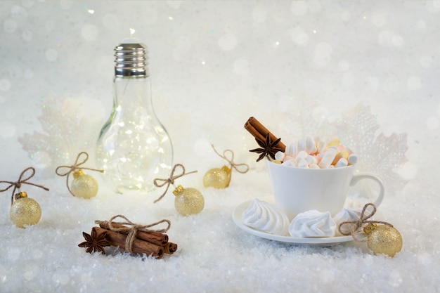 Tazza della bevanda calda con la caramella gommosa e molle e le spezie su neve.