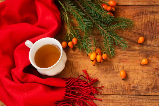 A cup of hot black tea with a red scarf rose berries and spruce on a wooden background