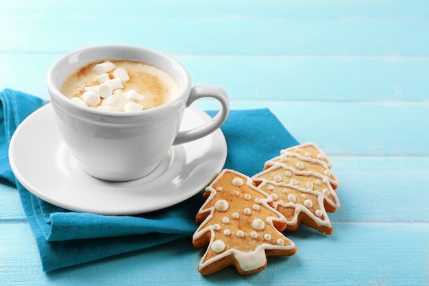 Cup of hot cacao with marshmallow, cookies and napkin on blue table