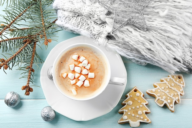 Cup of hot cacao with marshmallow, cookies and warm scarf on blue table