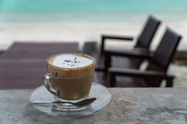 Cup of hot cappuccino on terrace and blurred desk on sea beach.