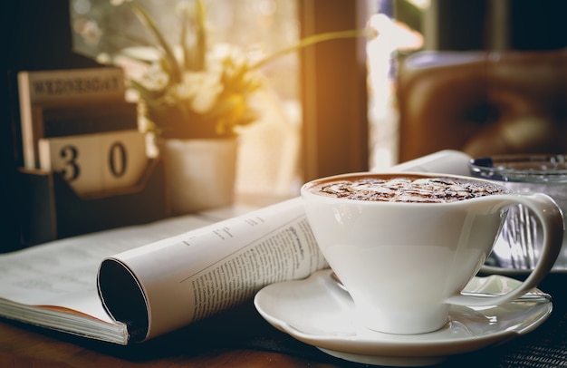 Cup of hot cappuccino with newspaper and calendar