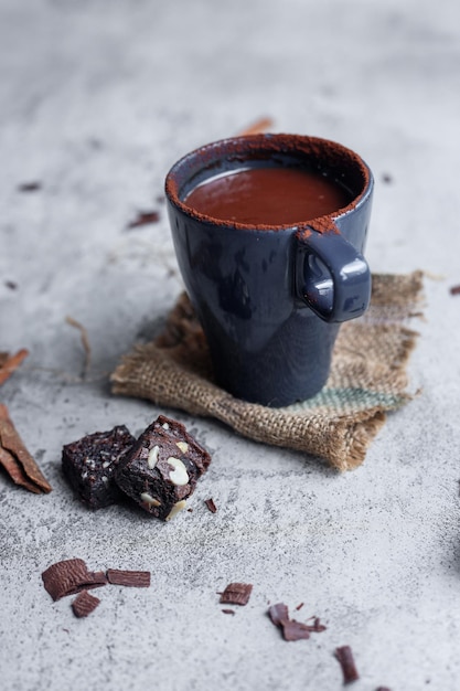 Cup of hot chocolate and pieces of chocolate brownie on light concrete background