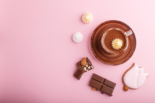 Cup of hot chocolate and pieces of milk chocolate with almonds on pink background. top view.