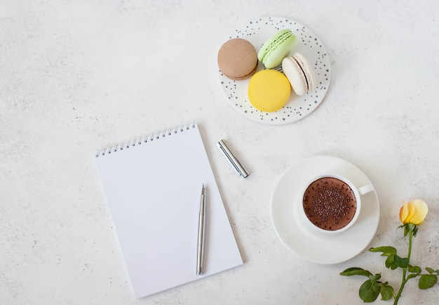 Cup of hot chocolate with macarons, flower and notepad