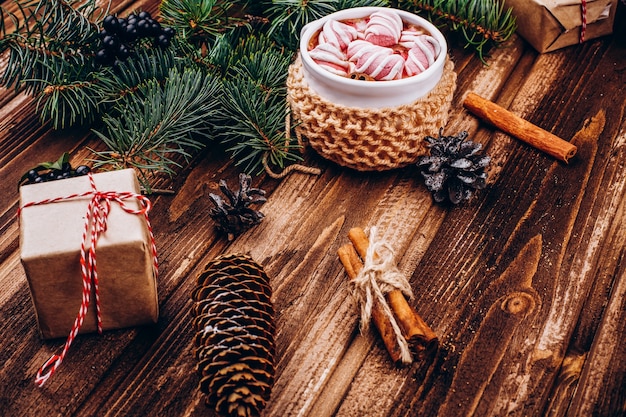 Cup of hot chocolate with marshmallows, cinnamon, cones and fir tree branches on the wooden table 