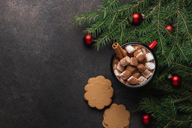Чашка горячего какао с зефиром, корицей и имбирными печенье, окруженная рождественской елей