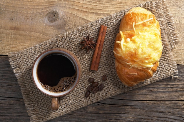 Cup of hot coffee and croissant with cheese for breakfast on old wooden table top view