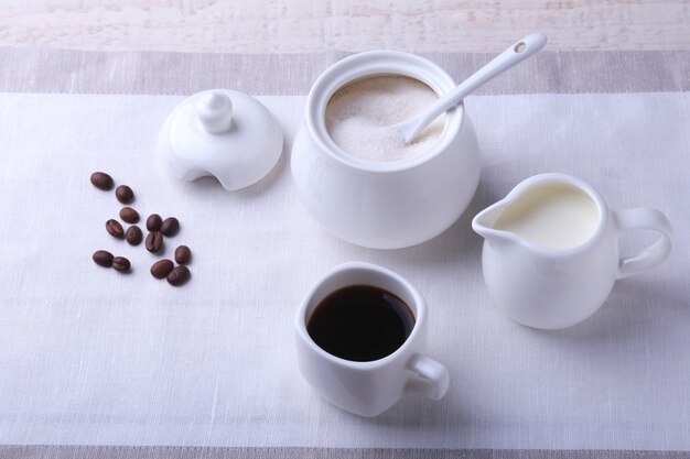 Tazza di caffè caldo, chicchi di caffè, brocca di latte e scodella con zucchero. concetto di caffè.