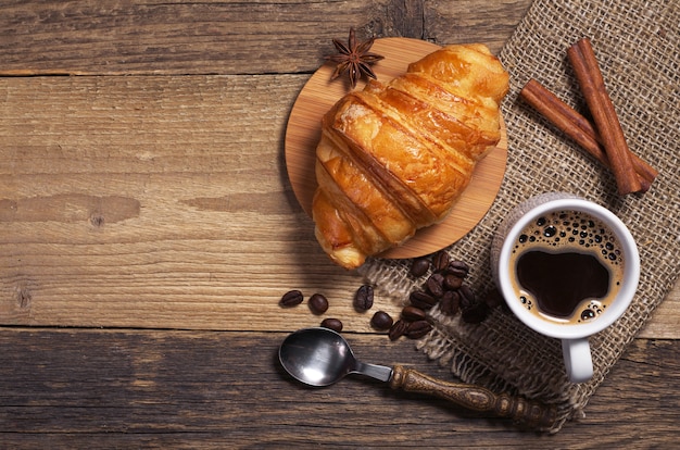 Cup of hot coffee and fresh croissant on old wooden table