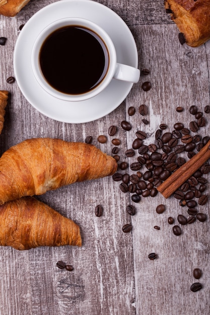 Tazza di caffè caldo e croissant appena sfornati sul tavolo di legno scuro. croissant gustoso.