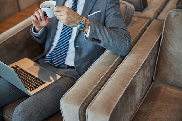 Cup of hot coffee in hands of stylish businessman