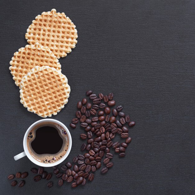 Cup of hot coffee and homemade waffles on black stone background, top view with space for text