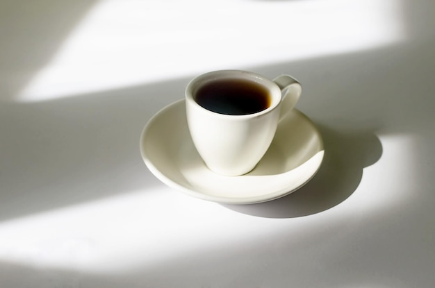 Чашка горячего кофе в лучах утреннего солнца на белом столе