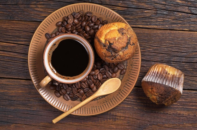 오래된 나무 탁자 위에 있는 접시에 잼을 넣은 뜨거운 커피와 머핀 한 잔
