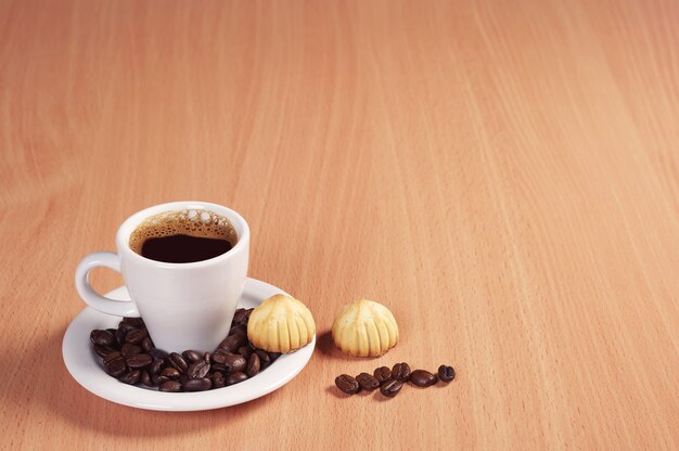 Cup of hot coffee and small cookies on desk