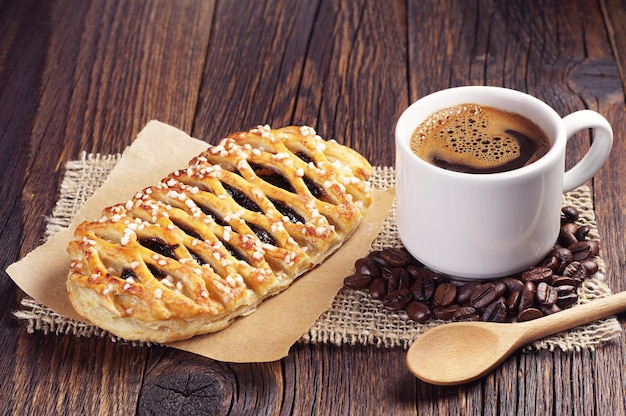 Cup of hot coffee and sweet bun with jam on dark wooden table