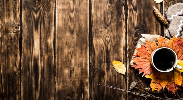 Cup of hot coffee with autumn leaves. On wooden background.