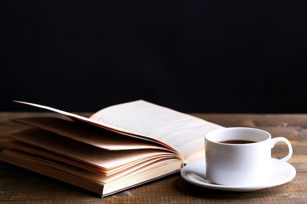 Cup of hot coffee with book on table on dark background