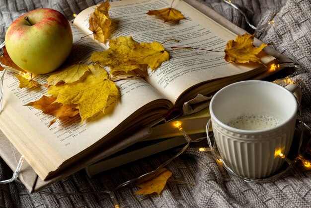 Photo a cup of hot coffee with cream, books, an apple and yellow maple leaves