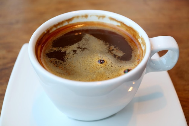 Una tazza di caffè caldo con superficie schiumosa isolata sul tavolo di legno
