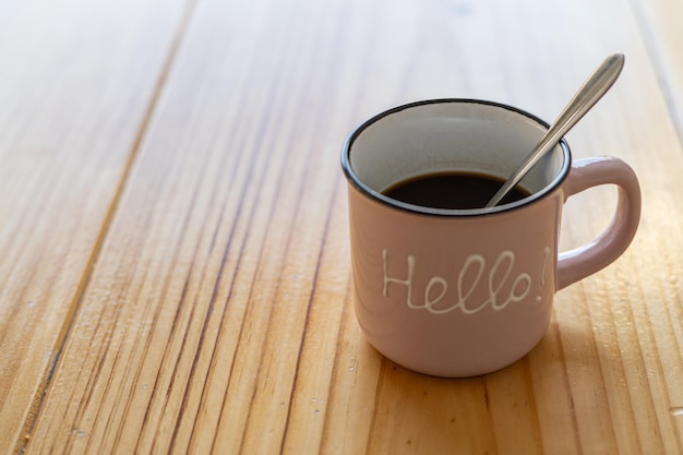 Cup of hot coffee on a wooden table outside the house with a message with the word Hello