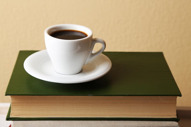 Cup of hot drink on book on light wall background