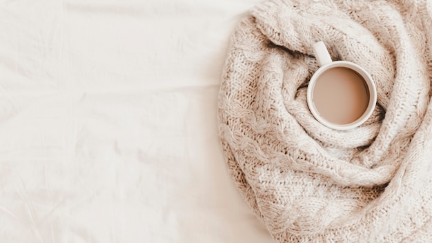 Cup of hot drink in plaid on bedsheet 