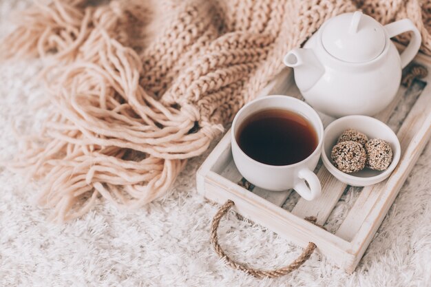 Cup of hot drink and teapot on a serving tray, knitting clothes