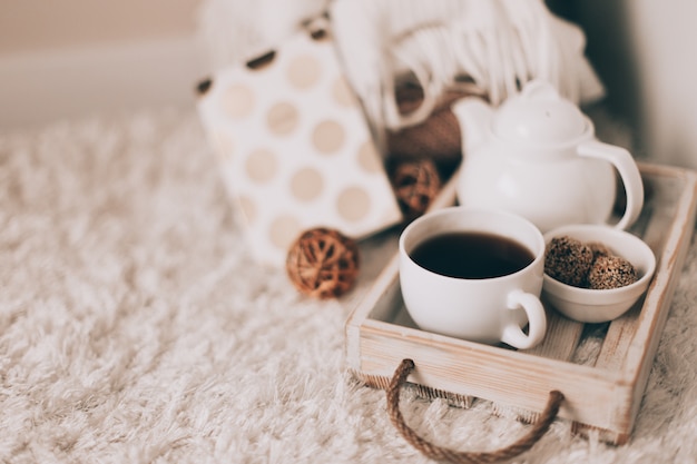 Cup of hot drink and teapot on a serving tray, knitting clothes