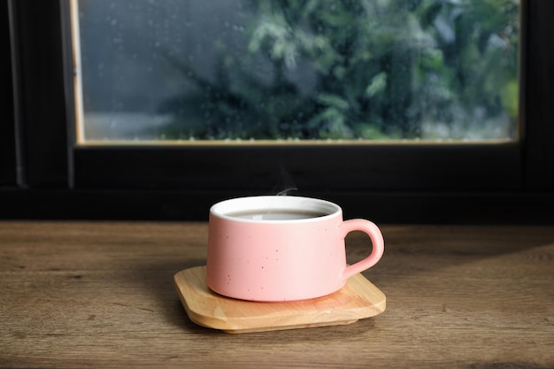 Cup of hot drink on window sill against glass with rain drops space for text