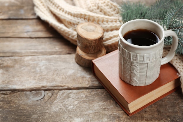 Cup of hot drink with knitted warm winter scarf on old wooden table