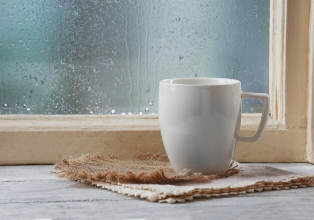 Photo cup of hot drink with napkin on windowsill on rain background