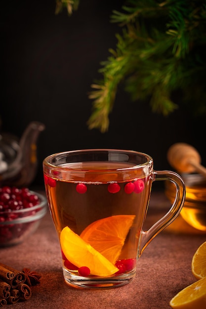 Cup of hot healthy vitamin tea made of cranberries, lemon slices and honey served on brown table