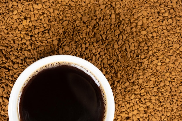 A cup of hot instant coffee on a background of freezedried granules