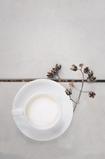 Foto tazza di latte caldo caffè d'arte sul pavimento di legno sfondo di colore bianco e fiori secchi, in vista dall'alto.