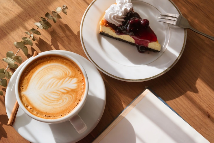 Photo コーヒーショップカフェで本を持つ木製のテーブルの上のホットラテアートコーヒーのカップ。