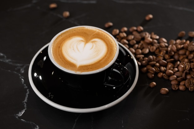 Cup of hot latte coffee with beautiful milk foam latte art texture with coffee bean on black marble background. Overhead view, copy space. Advertising for cafe menu. Coffee shop menu.