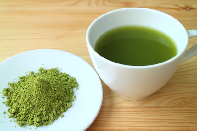 Una tazza di tè verde matcha caldo con un piccolo piatto di polvere di tè matcha