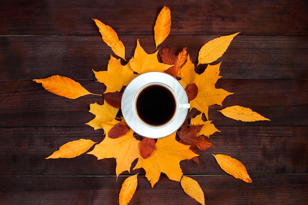 Cup of hot strong coffee and fallen leaves on wooden background Hello autumn concept Warm beverage for cold weather