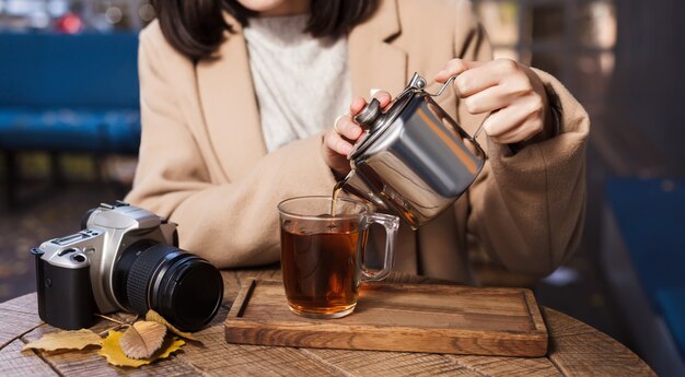 A cup of hot tea, a camera and yellow leaves closeup. Autumn background. Girl's hands