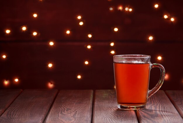 Photo cup of hot tea drnk on wooden table. christmass lights on background