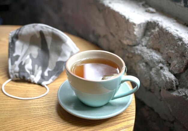 Cup of hot tea and face mask on wood table