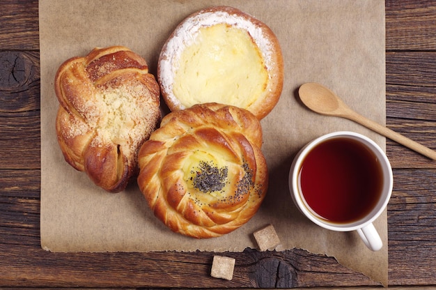 Cup of hot tea and fresh buns on rustic wooden table, top view