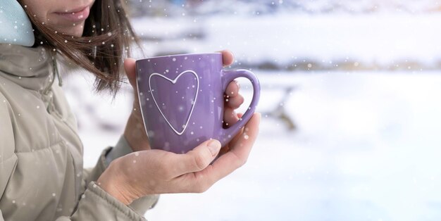 A cup of hot tea in hands against the background of white snow